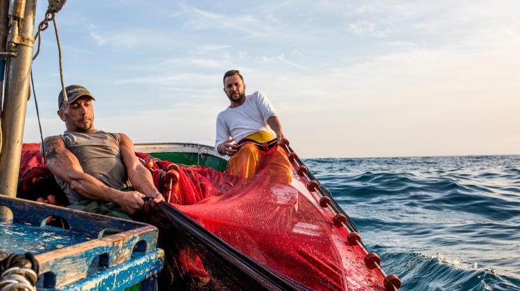 Two fishers on a boat pull fishing gear through open water.