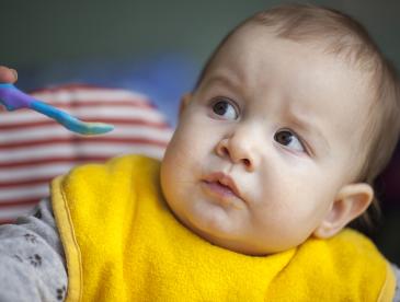 A baby refusing to eat from an offered spoon